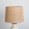Pantalla de rafia natural cónica mediana de Mahe Homeware, con ribete crema sobre una base blanca.