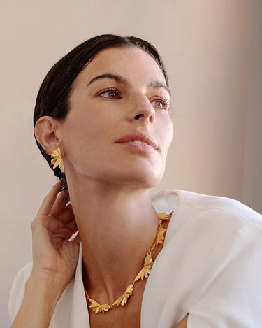 Par de pendientes de Joidart: modelo con pendientes dorados desplegados y un collar adicional a juego sobre camisa blanca.