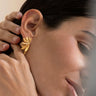 Par de pendientes dorados de formas desplegadas de Joidart: pendiente dorado de elementos alargados desplegados como abanico puesto en el lóbulo; mano junto al cabello.