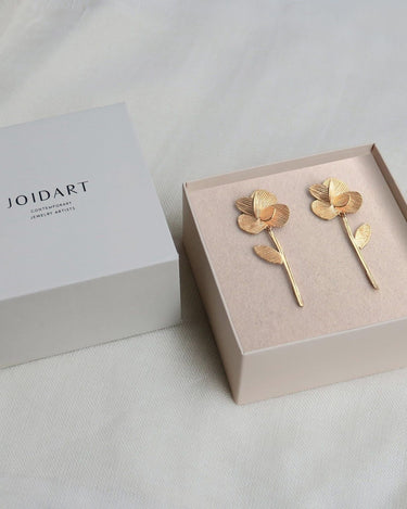 Par de pendientes dorados largos de flor y tallo en caja clara con tapa Joidart.