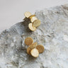 Par de pendientes dorados medianos de discos de Joidart: dos pendientes dorados pequeños formados por discos agrupados, sobre una piedra gris.