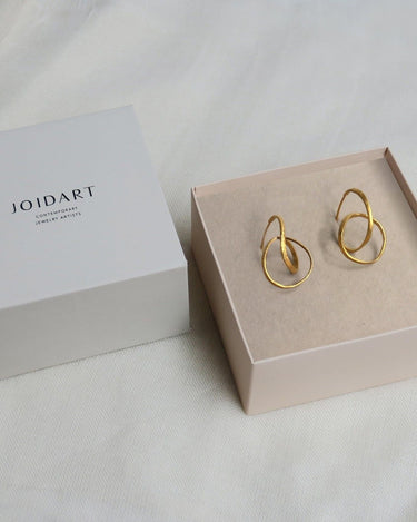 Dos pendientes dorados medianos de cintas entrelazadas en caja clara con tapa Joidart.