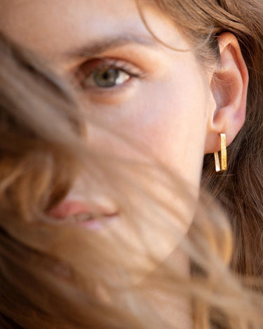 Acercamiento al rostro de una modelo con aro dorado rectangular estrecho.