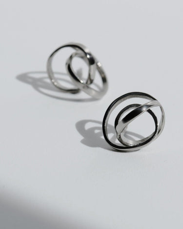 Par de pendientes de plata pequeños entrelazados de Joidart: dos pendientes pequeños plateados de cintas entrelazadas sobre fondo gris con sombras.