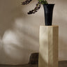Pedestal de hormigón blanco roto de Ferm Living con jarrón negro y flores encima.