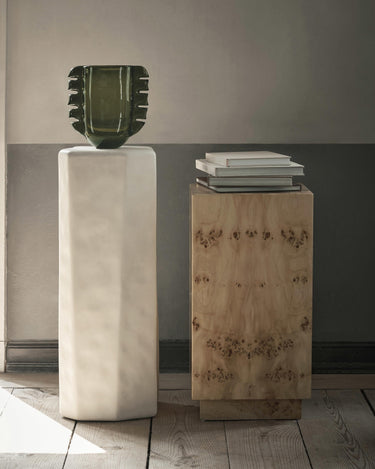 Pedestal Staffa blanco roto junto a un pedestal de madera de otra colección.