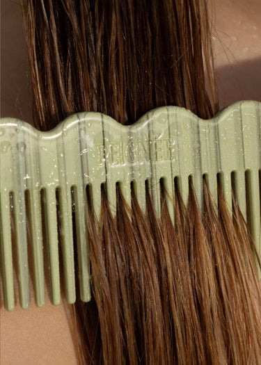 Peine de acetato verde salvia de contorno ondulado de Peignée Paris, entre el cabello.