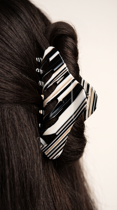 Pinza de pelo lateral de acetato a rayas negras y crema de Peignée Paris, sujetando un recogido.