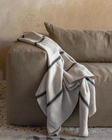 Plaid beige de lino y lana de Bed and Philosophy, sobre el brazo de una butaca