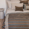 Plaid de lana y lino a rayas en tonos tierra de Bed and Philosophy, extendido sobre una cama con cojines de rayas