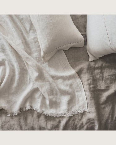 Plaid de lino blanco con flecos, textiles blancos sobre una cama, vistos desde arriba