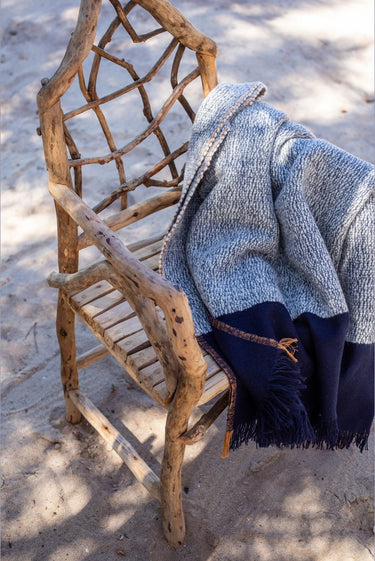 Plaid Haika azul y crudo con flecos, colocado sobre un sillón de fibras