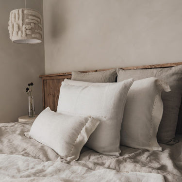 Plaid de lino blanco con flecos sobre una cama con cojines de Bed and Philosophy