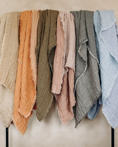 Plaids de lino gofrado de Le Monde Sauvage en varios colores, colgados en una barra