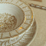 Plato hondo de gres con arcos pintados en beige de Leandro Cano: detalle de plato hondo pintado sobre plato llano en una mesa.