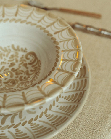 Plato hondo de gres con arcos pintados en beige de Leandro Cano: detalle de plato hondo pintado sobre plato llano en una mesa.
