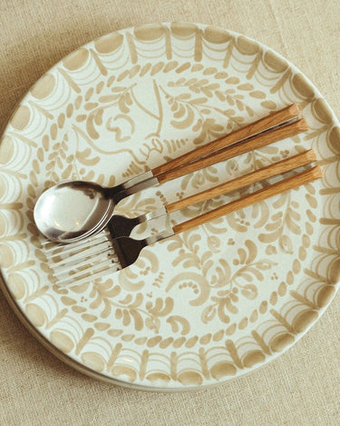 Plato llano de gres con arcos pintados en beige de Leandro Cano: plato llano con arcos beige y cubiertos con mangos de madera.