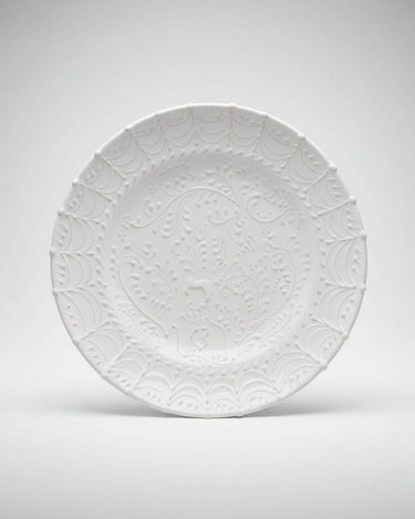 Plato llano de gres blanco con relieves de arcos de Leandro Cano: plato llano blanco apoyado de pie, con arcos y motivos vegetales en relieve.