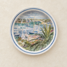 Plato de pared vintage pintado a mano, de cerámica blanca con paisaje portuario y borde azul, colgado sobre pared crema