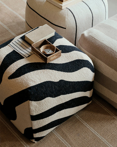 Puf gris claro y beige de Broste Copenhagen junto a una mesa auxiliar