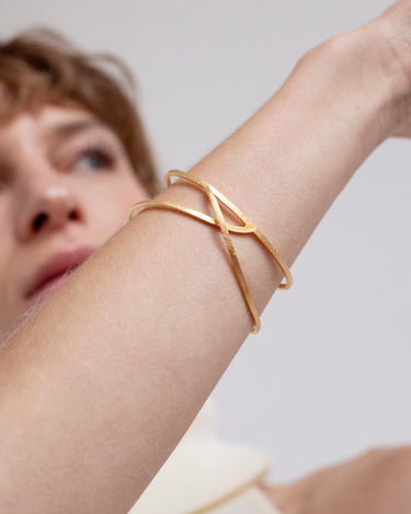 Pulsera de Joidart: detalle de pulsera dorada puesta, con muñeca levantada y rostro desenfocado detrás.