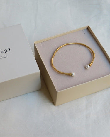Una de las pulseras doradas Eclat de Joidart, con dos extremos blancos, dentro de una caja clara.