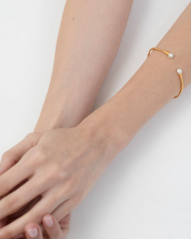 Pulsera de Joidart: pulsera dorada sinuosa con dos extremos blancos puesta en muñeca.