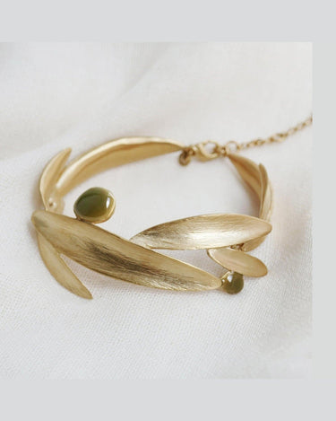 Pulsera de hojas doradas con esmalte verde oliva de Joidart: pulsera dorada formada por hojas alargadas y pequeños elementos redondos verde oliva, sobre tejido blanco; se ven cierre de mosquetón y cadena.