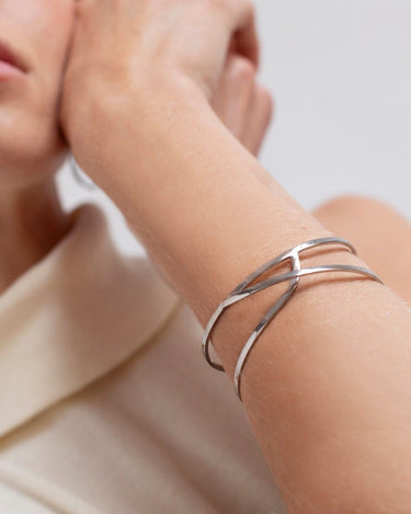 Pulsera plateada puesta en muñeca, con la mano apoyada junto al rostro.
