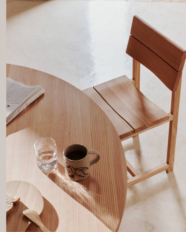 Detalle de asiento y respaldo de madera junto a mesa con taza.