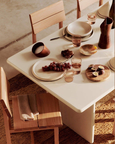 Silla de madera junto a mesa clara con plato, uvas y vaso ámbar.