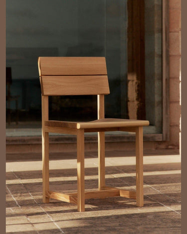 Silla de comedor de abeto Douglas macizo de Ferm Living: silla de madera en terraza de piedra; respaldo formado por dos tablas horizontales.