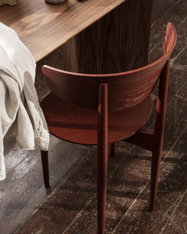 Silla de Ferm Living: detalle posterior del respaldo rojizo junto a mesa de madera oscura.