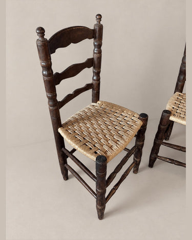 Detalle de una silla de madera oscura con asiento de fibra trenzada y segunda silla parcial a la derecha
