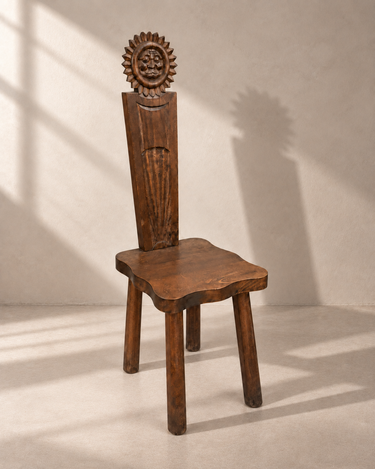 Silla de madera marrón con respaldo de sol tallado y asiento ondulado, vista en tres cuartos