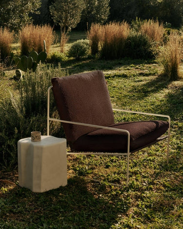 Sillón de exterior en bouclé marrón de Ferm Living con estructura beige en el jardín.