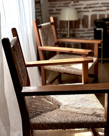 Conjunto de sillones vintage de madera con asiento y respaldo trenzados, detalle junto a una ventana
