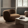 Sofá curvo derecho de tejido de lana ocre de Ferm Living: ambiente interior junto a ventana: sofá curvo marrón ocre con mesa baja rectangular clara y alfombra; costado redondeado prominente.