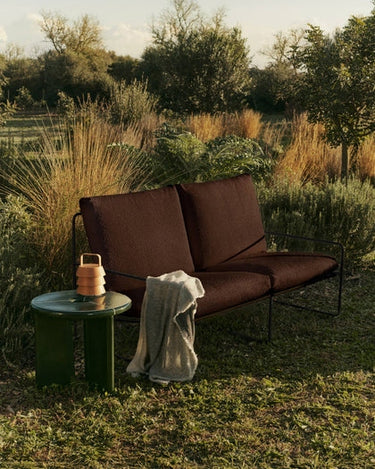 Sofá de Ferm Living en un jardín con mesa auxiliar y jarrón decorativo.