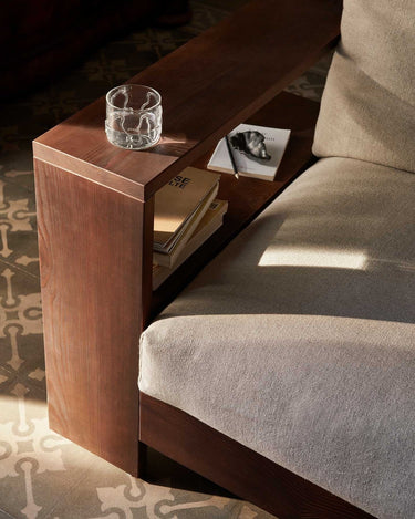 Detalle del brazo de uno de los sofás de Ferm Living, con una balda, libros y un vaso.