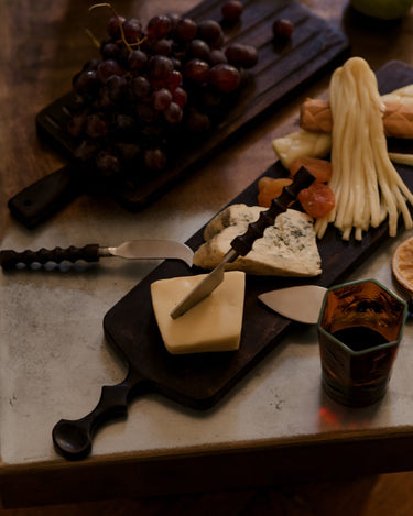 Tabla Zander marrón oscuro con uvas y quesos entre otros utensilios de servir