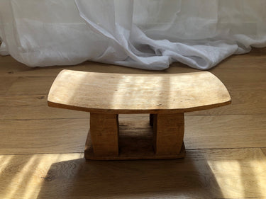 Taburete apoyacuellos de madera junto a cortinas blancas con luz natural