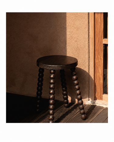Taburete de madera de mango oscura de Bazar Bizar, junto a una puerta de madera