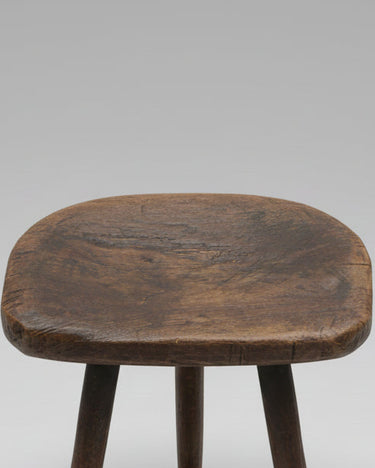 Detalle de taburete rústico de ordeño con asiento de madera natural