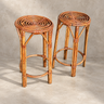 Dos taburetes altos vintage de bambú marrón con asiento calado sobre fondo de cemento topo claro