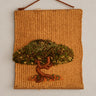 Tapiz de árbol en relieve con fibras verdes y marrones, colgado de cordón sobre pared topo