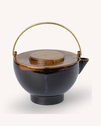 Composición de mesa con tetera de cerámica marrón flameada con asa de latón en uso