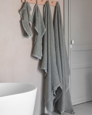 Toalla color eucalipto en un baño de materiales naturales