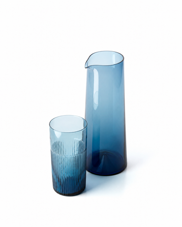 Vaso alto de vidrio azul ondulado, junto a una jarra de vidrio azul