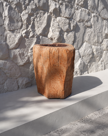 Vela recargable de tronco de madera natural de Bazar Bizar, junto a una pared de piedra